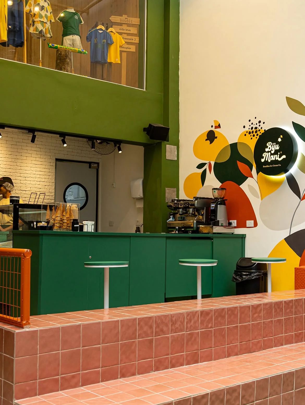 Pop-up store Biju Mania em Pinheiros com balcão verde em marcenaria, banco revestido de cerâmica e mural colorido